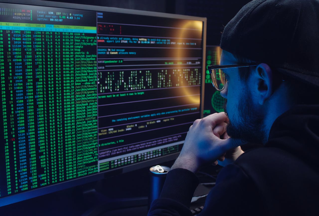 Services-02 Man intently working on computer programming with code displayed on dual monitors in a dimly lit room.