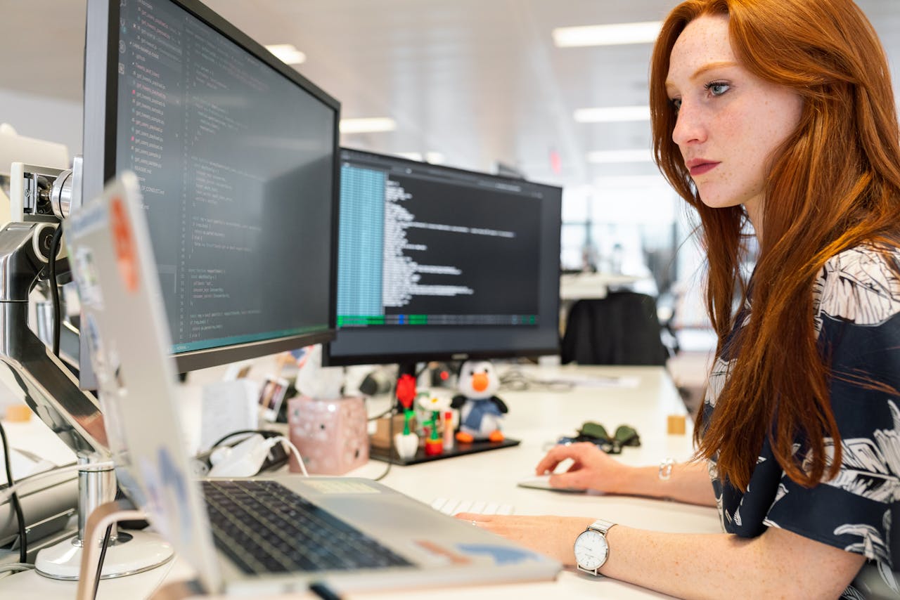 creative A focused female software engineer coding on dual monitors in a modern office.